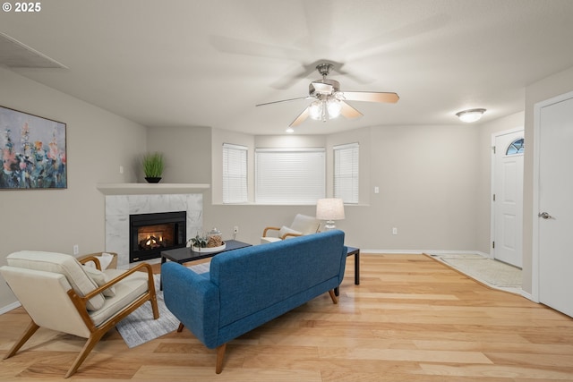 living room featuring ceiling fan, a premium fireplace, and light hardwood / wood-style flooring