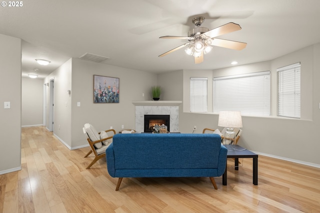 living room with a high end fireplace, ceiling fan, and light wood-type flooring