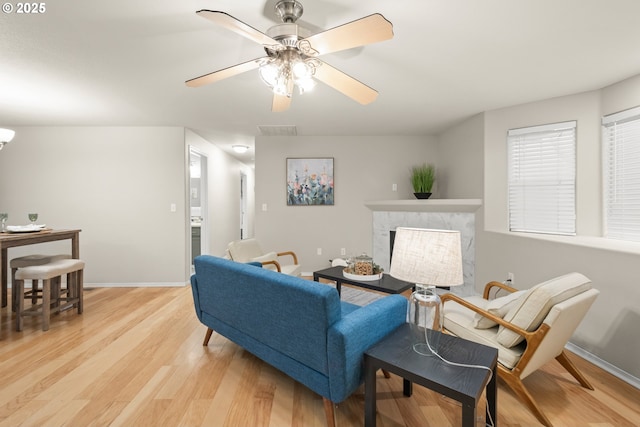 living room featuring a high end fireplace, light hardwood / wood-style floors, and ceiling fan