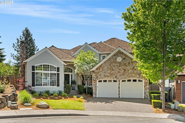 traditional-style home with stone siding, driveway, an attached garage, fence, and a chimney