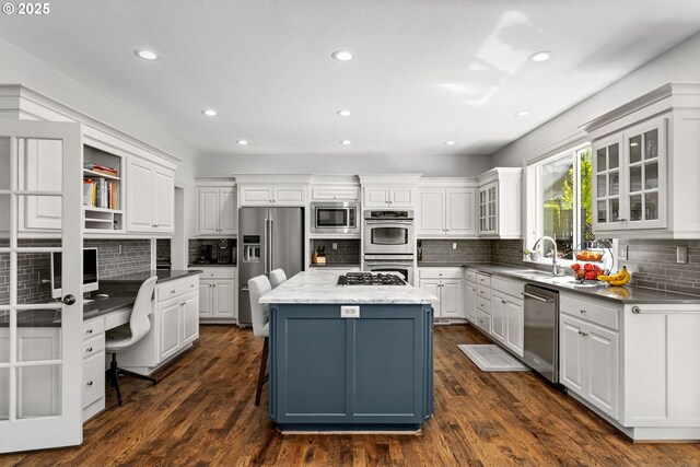 kitchen with stainless steel appliances, a sink, white cabinets, a kitchen island, and backsplash