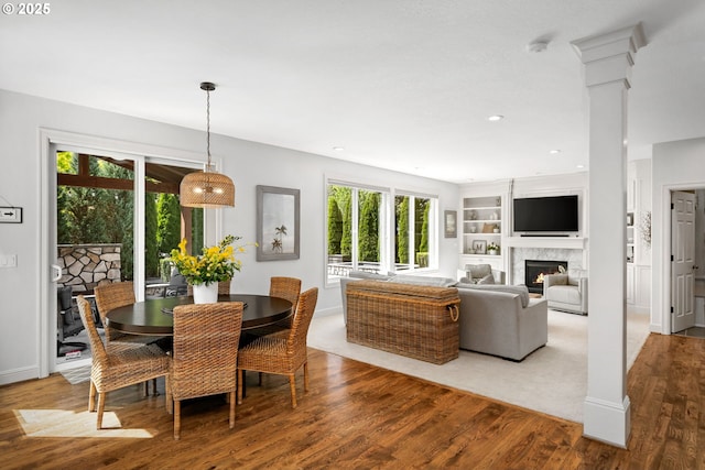 dining space with wood finished floors, a premium fireplace, baseboards, recessed lighting, and decorative columns