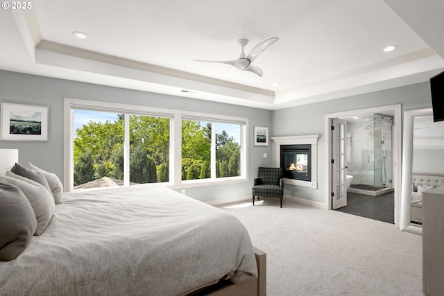 bedroom with a raised ceiling, carpet floors, recessed lighting, baseboards, and a glass covered fireplace