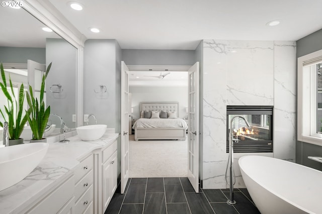 full bathroom featuring ensuite bath, recessed lighting, double vanity, a soaking tub, and a premium fireplace