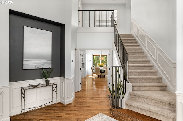 entryway with wood finished floors, stairway, a decorative wall, wainscoting, and a towering ceiling