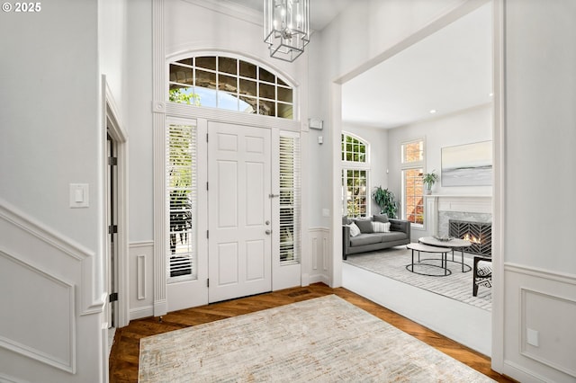 foyer with a chandelier, a wainscoted wall, a premium fireplace, wood finished floors, and crown molding