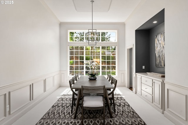 carpeted dining area featuring a decorative wall, wainscoting, and ornamental molding