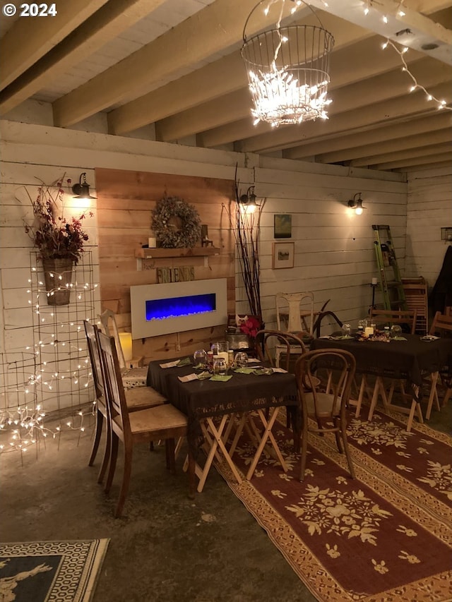 dining room featuring wooden walls, concrete flooring, a chandelier, beam ceiling, and a fireplace