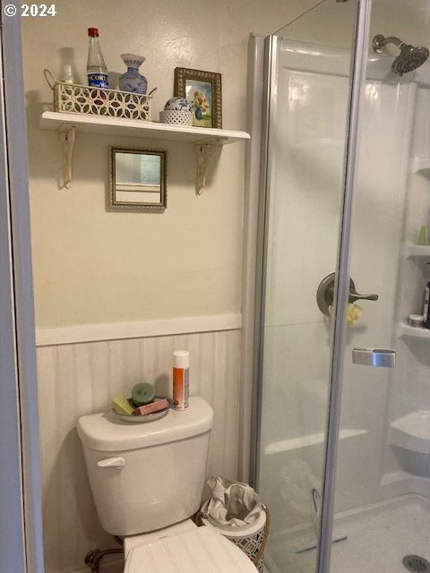 bathroom with a stall shower, wainscoting, and toilet