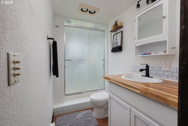 bathroom featuring wood-type flooring, toilet, vanity, decorative backsplash, and an enclosed shower