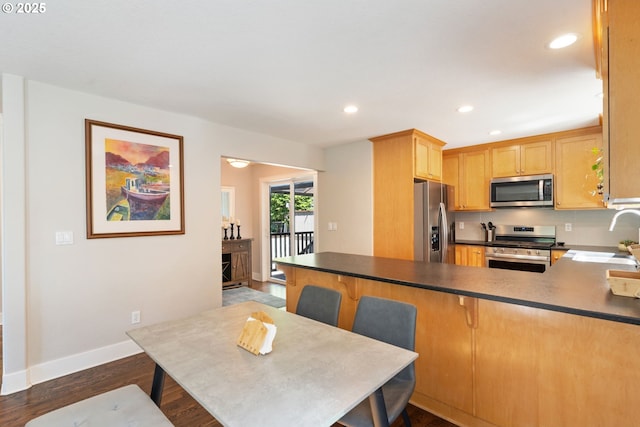 511 NE Skidmore St, Portland, OR 97211 - kitchen with appliances with stainless steel finishes, recessed lighting, a peninsula, dark wood-style flooring, and a kitchen bar