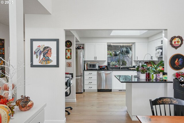 kitchen featuring stainless steel appliances, a skylight, white cabinets, light hardwood / wood-style flooring, and sink