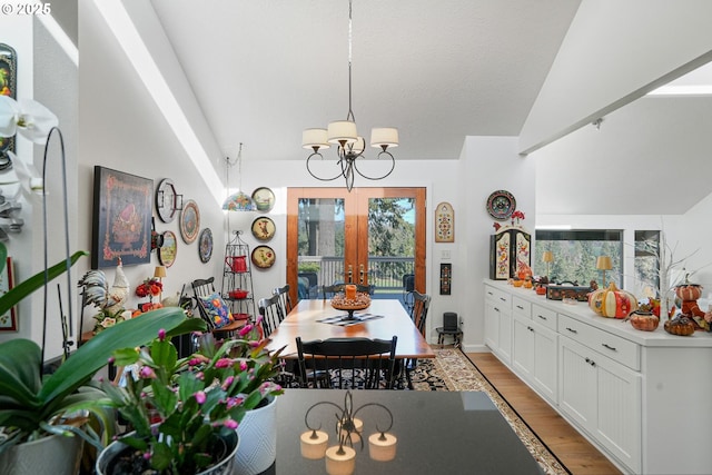 dining room with light wood-type flooring, lofted ceiling, french doors, and a notable chandelier