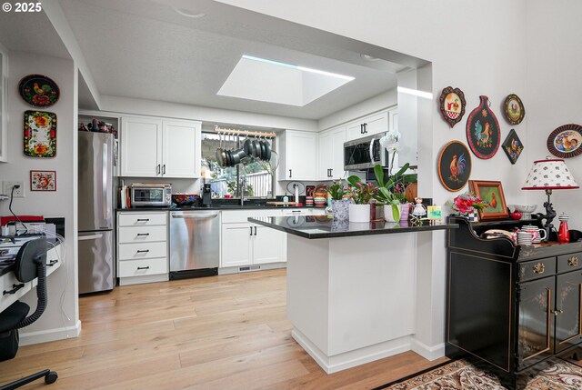 kitchen with stainless steel appliances, white cabinets, light wood-type flooring, kitchen peninsula, and a skylight