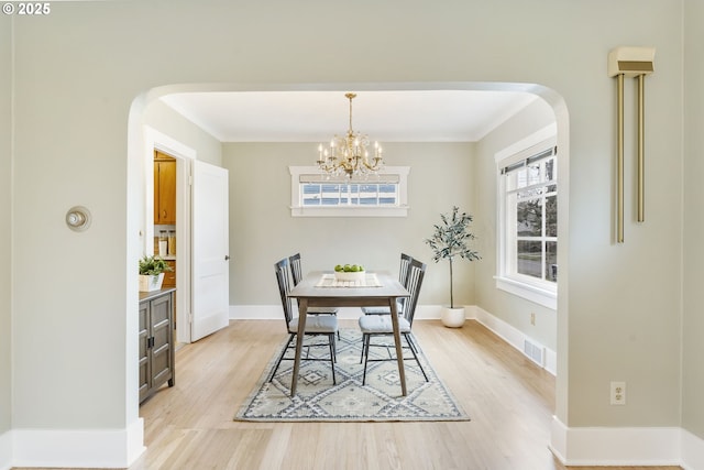 dining room featuring light wood-type flooring, arched walkways, visible vents, and baseboards