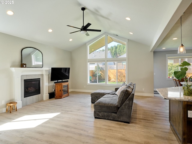 living room with light wood-style floors, a tiled fireplace, vaulted ceiling, and a wealth of natural light