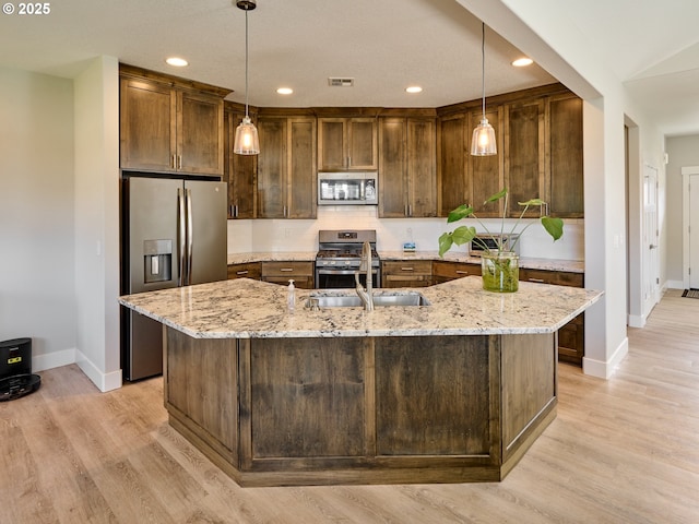 kitchen featuring appliances with stainless steel finishes, a center island with sink, visible vents, and light stone countertops