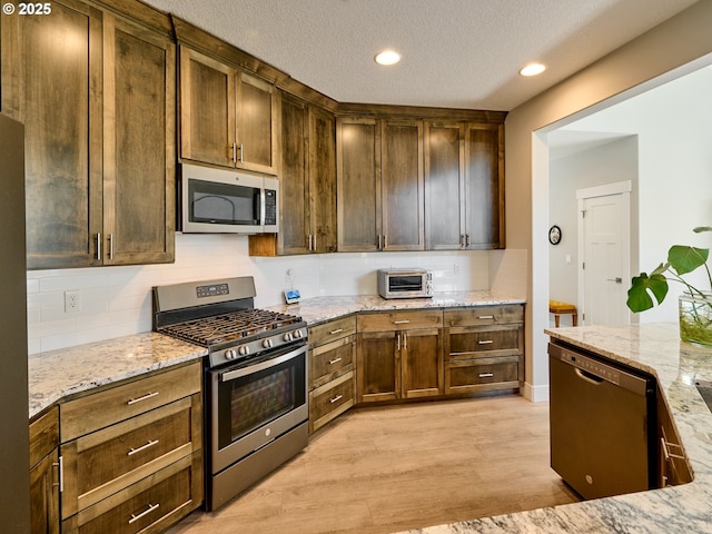 kitchen featuring appliances with stainless steel finishes, light wood-type flooring, backsplash, and light stone countertops