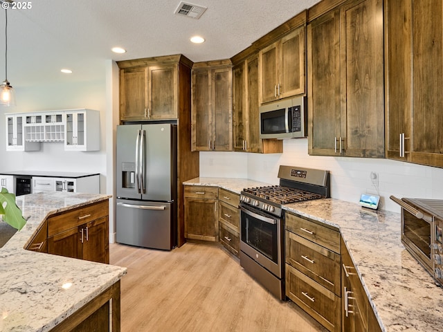 kitchen with stainless steel appliances, visible vents, backsplash, light stone countertops, and light wood-type flooring