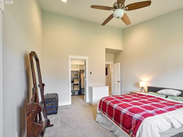 carpeted bedroom with a walk in closet, a closet, a high ceiling, ceiling fan, and baseboards