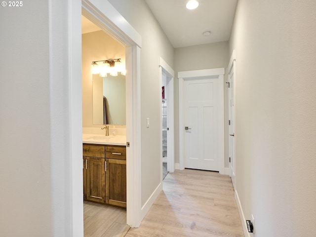 hallway with light wood-type flooring, a sink, and baseboards