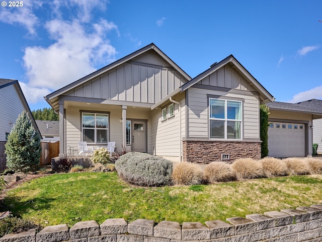 craftsman-style house featuring an attached garage, covered porch, stone siding, a front lawn, and board and batten siding