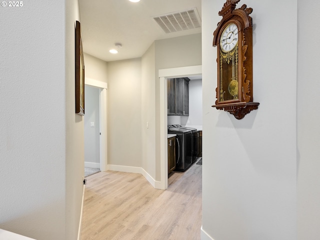 hallway featuring light wood finished floors, washing machine and dryer, visible vents, and baseboards