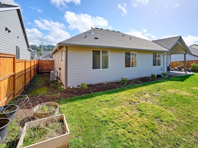 rear view of house with central AC unit, a vegetable garden, a lawn, a patio, and roof with shingles