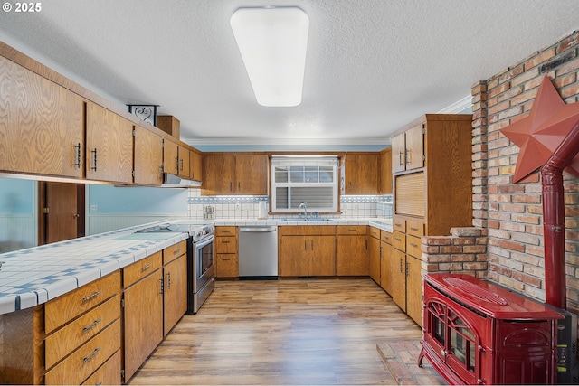 9065 Trask River Rd, Tillamook, OR 97141 - kitchen with stainless steel appliances, tile counters, light wood-style flooring, tasteful backsplash, and under cabinet range hood