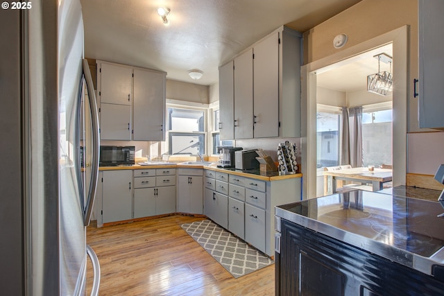 kitchen with stainless steel counters, decorative light fixtures, light hardwood / wood-style floors, sink, and stainless steel refrigerator