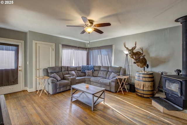 living room with ceiling fan, wood-type flooring, and a wood stove