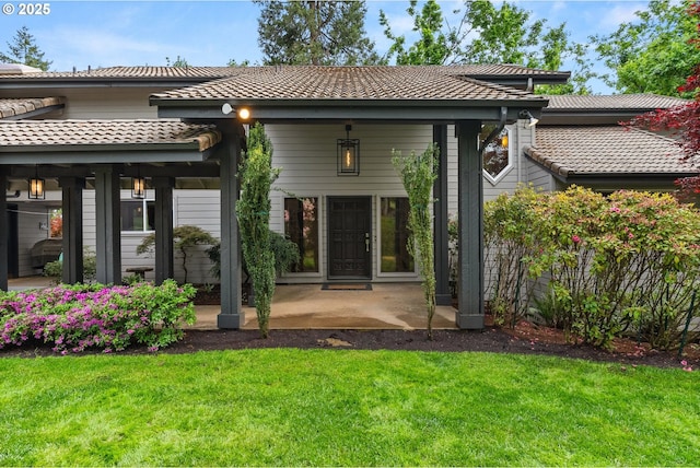 rear view of house featuring a yard, a tile roof, and a patio