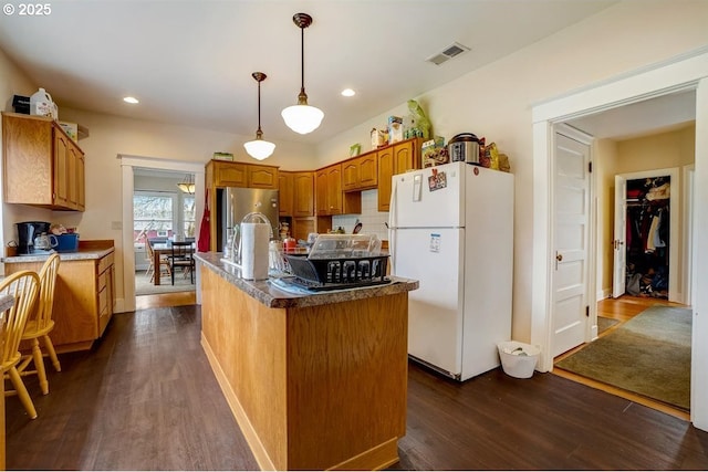 kitchen featuring dark wood-type flooring, decorative light fixtures, stainless steel refrigerator, an island with sink, and white fridge