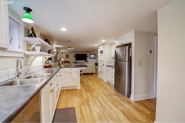 kitchen featuring sink, stainless steel refrigerator, white cabinetry, kitchen peninsula, and light wood-type flooring