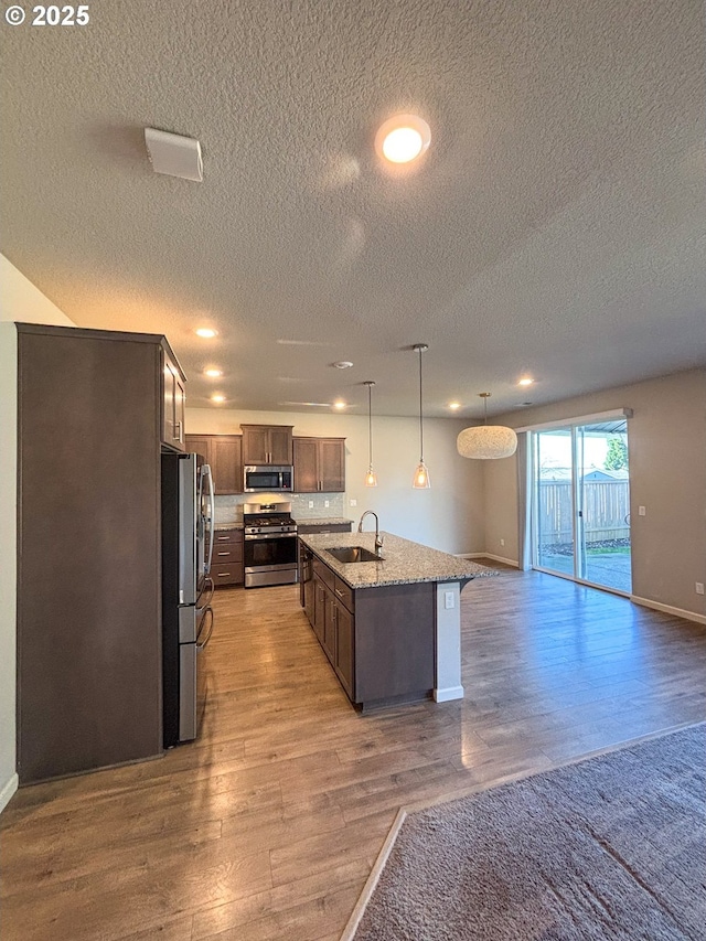 kitchen featuring wood-type flooring, an island with sink, sink, hanging light fixtures, and stainless steel appliances