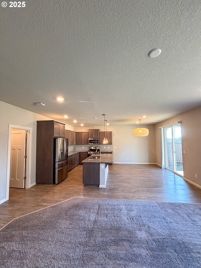 kitchen featuring sink, a kitchen island with sink, dark brown cabinets, stainless steel appliances, and decorative light fixtures