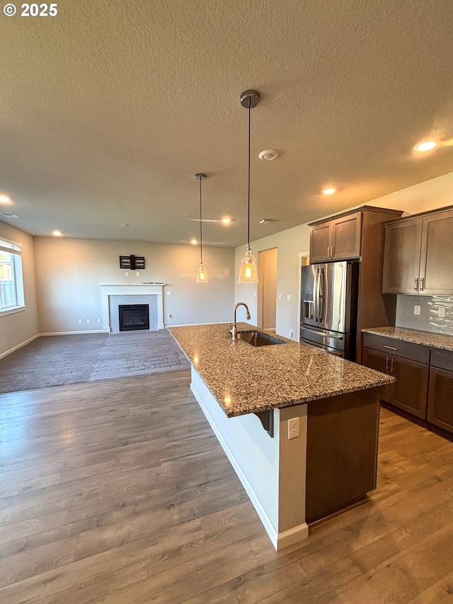 kitchen featuring sink, hanging light fixtures, a center island with sink, stainless steel fridge, and stone counters