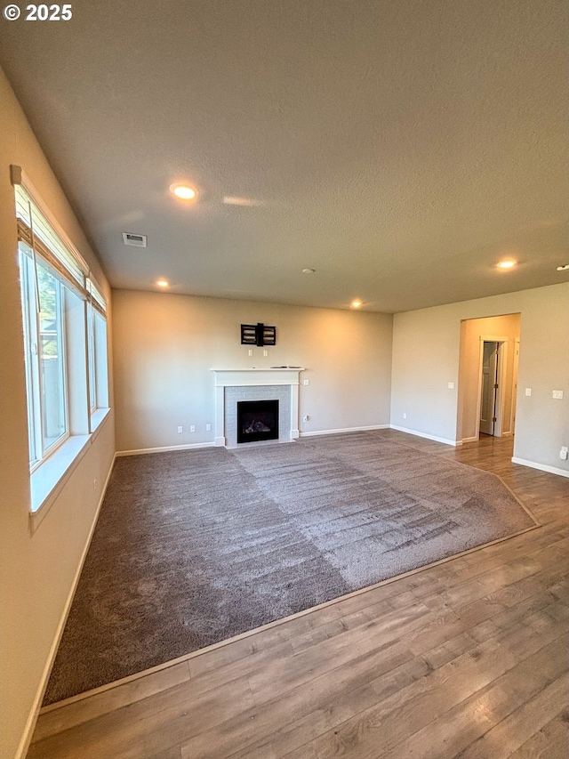 unfurnished living room featuring hardwood / wood-style floors, a brick fireplace, and a textured ceiling