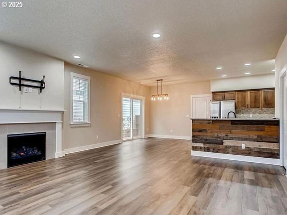 living room with a textured ceiling, a tile fireplace, recessed lighting, wood finished floors, and baseboards