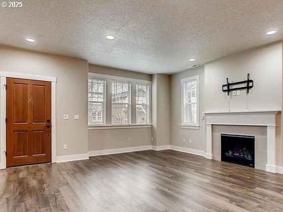 unfurnished living room with baseboards, a tile fireplace, wood finished floors, a textured ceiling, and recessed lighting