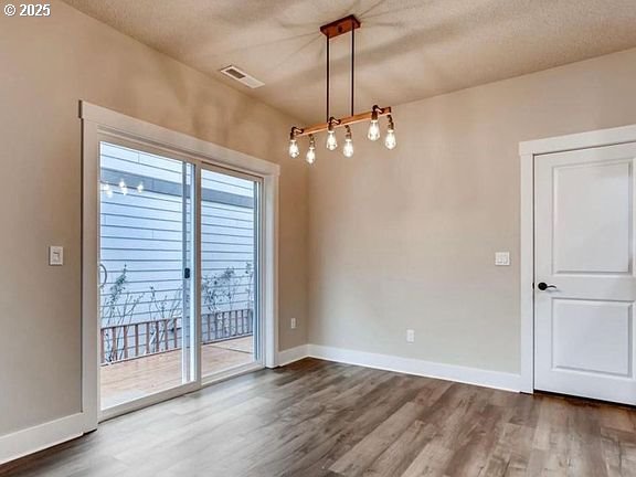 spare room with dark wood-style floors, a textured ceiling, visible vents, and baseboards