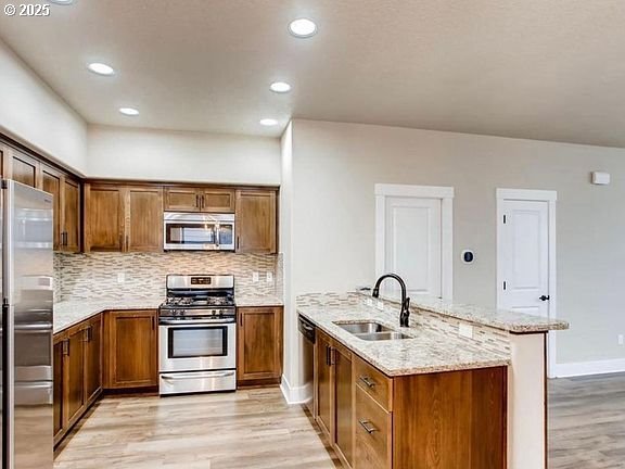 kitchen featuring stainless steel appliances, a sink, light stone countertops, light wood-type flooring, and a peninsula