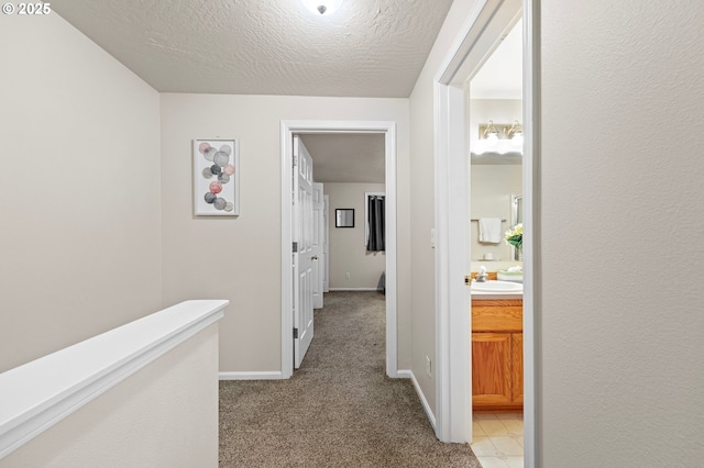 hallway featuring light carpet, sink, and a textured ceiling