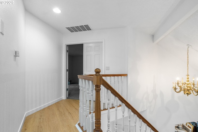 hallway with light wood-style flooring, baseboards, visible vents, a chandelier, and an upstairs landing