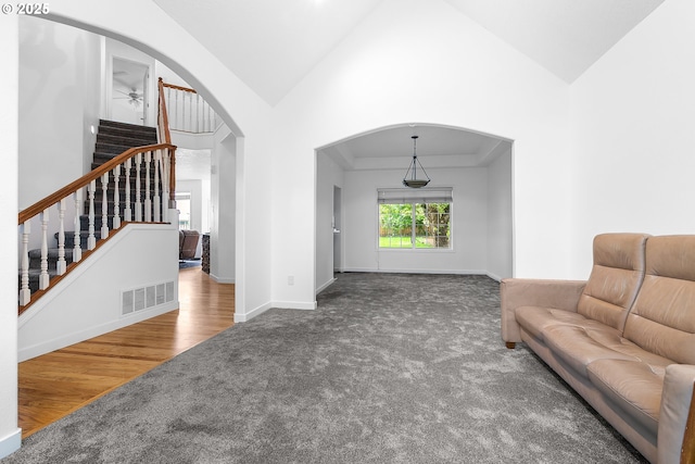 living room with carpet flooring, visible vents, stairs, vaulted ceiling, and arched walkways