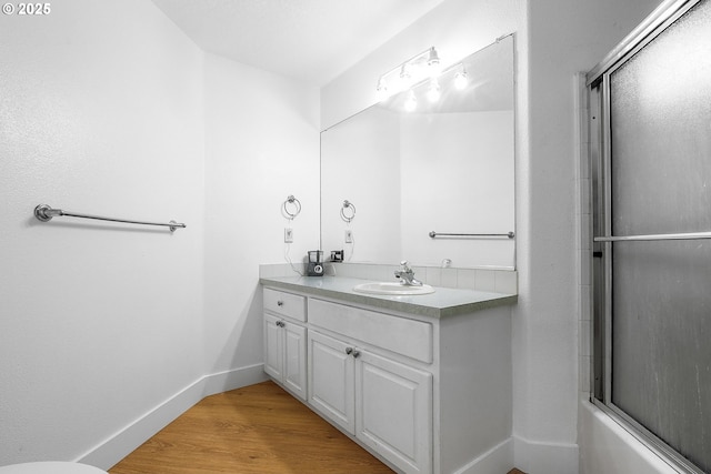 bathroom featuring enclosed tub / shower combo, vanity, baseboards, and wood finished floors