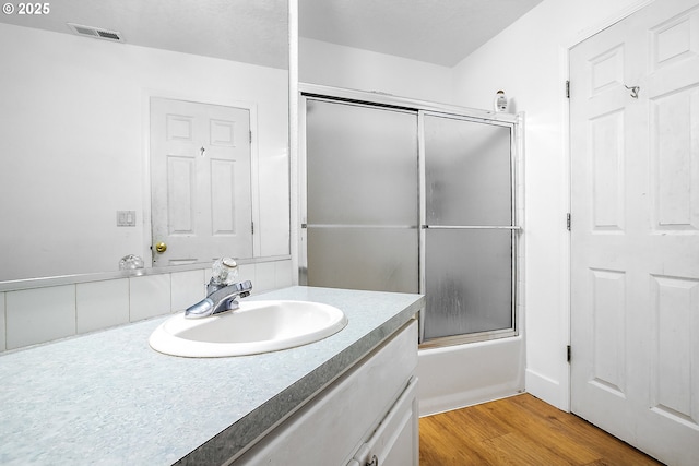 bathroom featuring visible vents, wood finished floors, vanity, and combined bath / shower with glass door