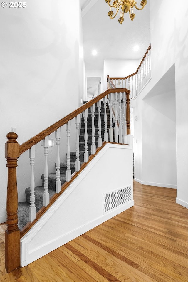 stairway featuring wood finished floors, a towering ceiling, visible vents, an inviting chandelier, and baseboards