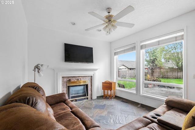 living room with stone tile flooring, baseboards, visible vents, ceiling fan, and a high end fireplace