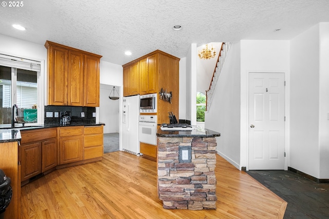 kitchen featuring light wood-style flooring, a sink, oven, brown cabinetry, and stainless steel microwave